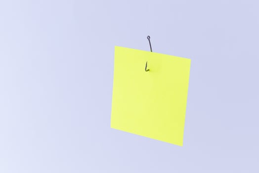 Mockup of a Blank Yellow Memo Paper with Copy Space Hanging on a Fishing Hook Against the White Background. Reminder or To Do List. Sticky Note Template photo