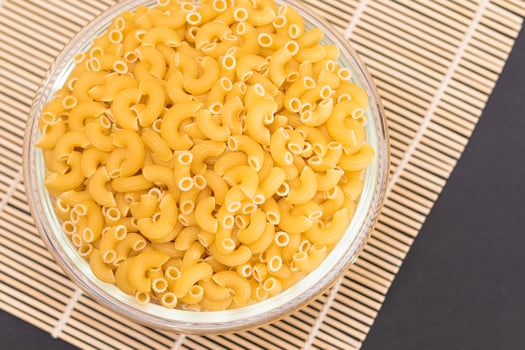 Uncooked Chifferi Rigati Pasta in Glass Jar on Bamboo Mat on Black Background. Fat and Unhealthy Food. Classic Dry Macaroni. Italian Culture and Cuisine. Raw Pasta photo