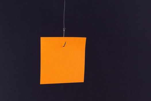 Mockup of a Blank Orange Memo Paper with Copy Space Hanging on a Fishing Hook Against the Black Background. Sticky Note Template photo