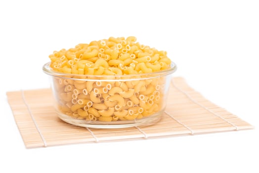 Uncooked Chifferi Rigati Pasta in Glass Jar on Bamboo Mat Isolated White Background. Fat and Unhealthy Food. Classic Dry Macaroni. Italian Culture and Cuisine. Raw Pasta - Isolation photo