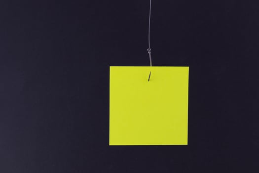 Mockup of a Blank Yellow Memo Paper with Copy Space Hanging on a Fishing Hook Against the Black Background. Reminder or To Do List. Sticky Note Template photo