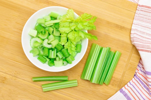 Fresh Chopped Celery Slices in White Bowl with Celery Sticks on Bamboo Cutting Board. Vegan and Vegetarian Culture. Raw Food. Healthy Diet with Negative Calorie Content photo