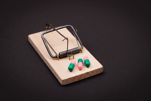 Pharmaceutical Addiction or Big Pharma Trap - Colored Pills or Capsules in Wooden Mousetrap on Black Background photo