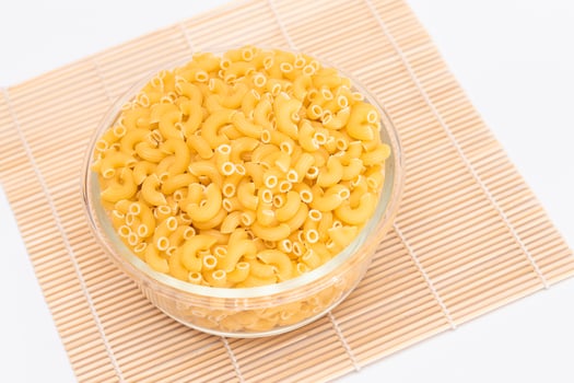 Uncooked Chifferi Rigati Pasta in Glass Jar on Bamboo Mat on White Background. Fat and Unhealthy Food. Classic Dry Macaroni. Italian Culture and Cuisine. Raw Pasta photo