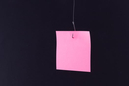 Mockup of a Blank Pink Memo Paper with Copy Space Hanging on a Fishing Hook Against the Black Background. Reminder or To Do List. Sticky Note Template photo