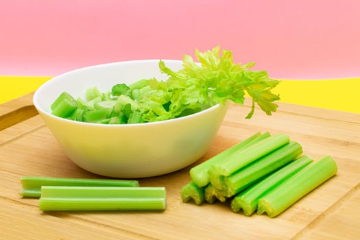 Fresh Chopped Celery Slices in White Bowl with Celery Sticks on Bamboo Cutting Board. Vegan and Vegetarian Culture. Raw Food. Healthy Diet with Negative Calorie Content photo