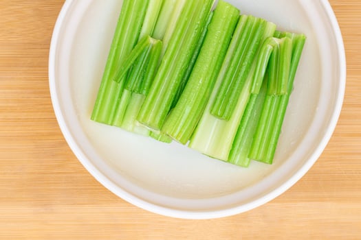 Fresh Chopped Celery Sticks with Water Drops in White Bowl on Bamboo Cutting Board - Top View. Vegan and Vegetarian Culture. Raw Food. Healthy Diet with Negative Calorie Content photo