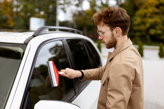 Young stylish man cleaning car window with squeegee photo