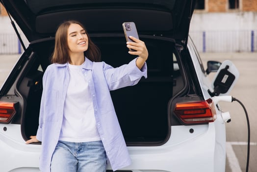 Young Woman Takes a Selfie Next to an Electric Car While Charging at a Modern Parking Lot photo