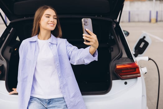 Young Woman Takes a Selfie Next to an Electric Car While Charging at a Modern Parking Lot photo