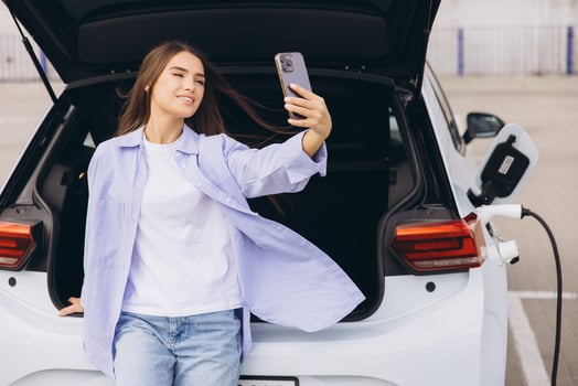 Young Woman Takes a Selfie Next to an Electric Car While Charging at a Modern Parking Lot photo