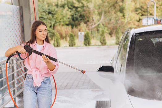 Woman Using Pressure Washer to Clean Her Car Outdoors photo
