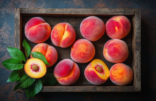 Fresh peaches in a wooden crate surrounded by green leaves on a rustic table photo