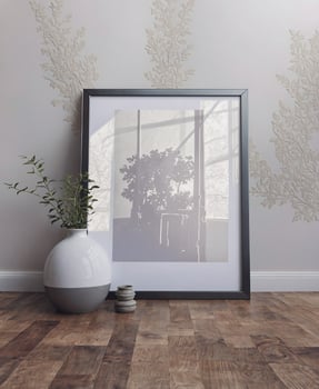 A framed photo of a plant on a table next to a vase