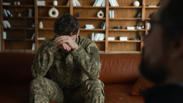 Upset depressed despair Caucasian male guy military soldier veteran camouflage uniform officer in pain holding head thinking sitting indoors with psychologist man mental health therapy session cabinet photo