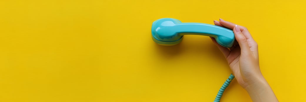 A vibrant blue telephone receiver held against a bright yellow background in a playful setting photo