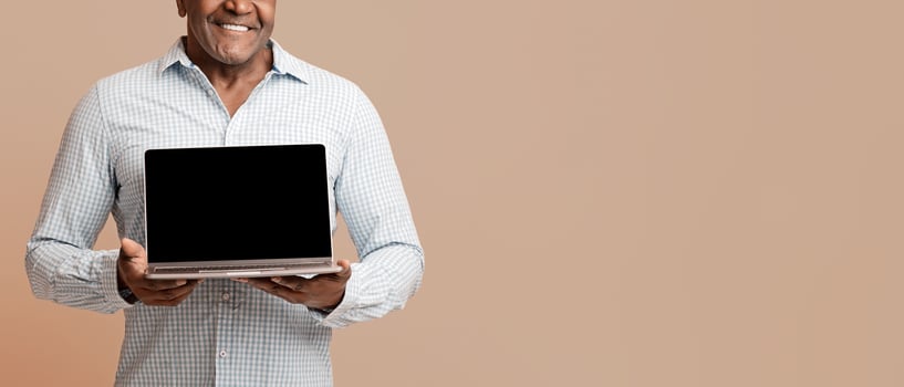 Modern lifestyle for old people. Mature african man showing blank screen of laptop, orange studio background photo