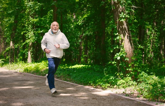 Elderly sporty man running in green forest during morning workout, copy space. Healthy and active lifestyle at any age concept photo
