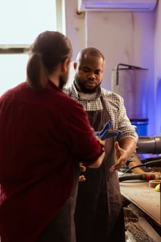 Master in woodworking shop giving BIPOC worker protection gloves before assembling furniture. Cabinetmaker preparing safety equipment for african american apprentice before starting work photo