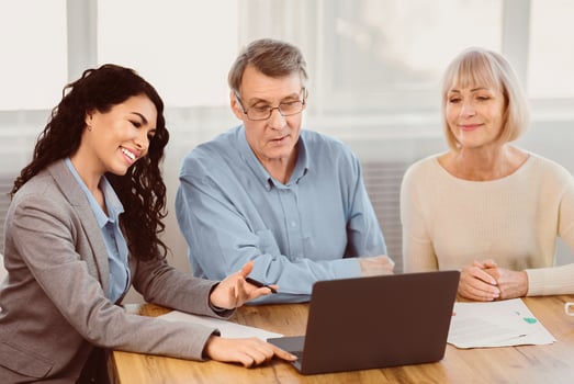 Real Deal. Older couple considering new home purchase talking with estate agent who showing them laptop photo
