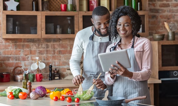 Modern technologies in everyday life. Black couple using digital tablet and cooking dinner in kitchen together, copy space photo