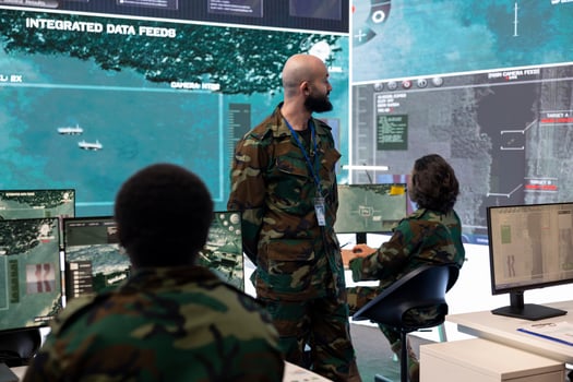 Trooper in camouflage uniform supervising surveillance systems in control room, ensuring operational success. Recruits team analyzing real time radar to support federal agency missions. photo