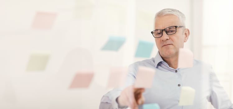 Pensive Mature Businessman In Glasses Putting Sticky Notes On Window At Office, Empty Space photo