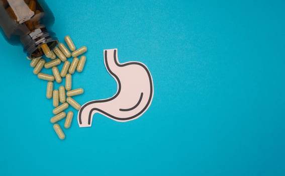 Stomach shape made from paper and pills capsules with a bottle on a blue background photo