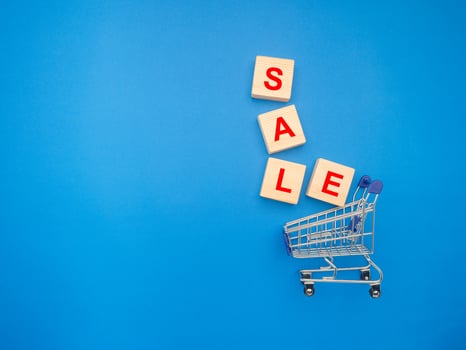 A miniature shopping trolley and wooden blocks with the word SALE over a blue background photo