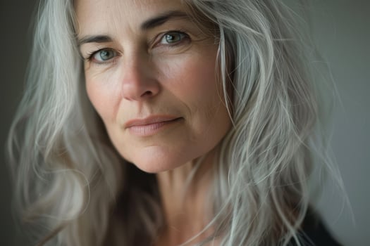 The mature woman gazes softly with her long gray hair framing her face, highlighting her expressive features in gentle natural light, conveying a sense of calm and introspection photo