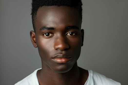 A youthful individual stands facing the camera, displaying a serene and contemplative expression. The simple backdrop emphasizes their features and the mood conveyed photo