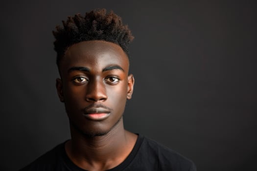 A young man stands confidently with a serious expression, highlighting his textured hairstyle against a dark, neutral background. The simplicity enhances his focused gaze photo