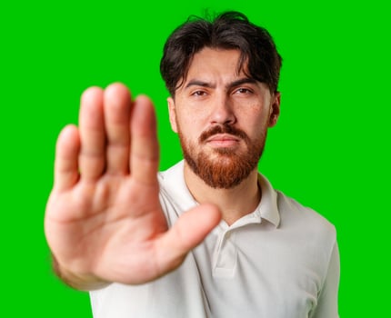 Man with a beard holding up his hand and looking at the camera against a bright green background photo