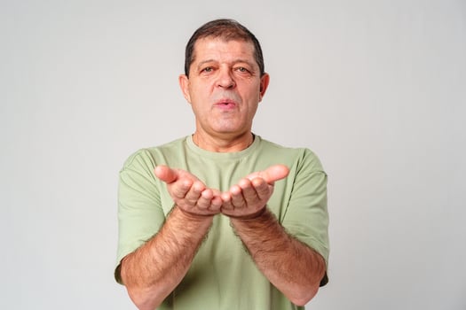 Elderly man demonstrating an open-handed gesture while standing against a plain background photo