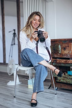 The photo shows a female photographer working in a studio environment. She is surrounded by professional equipment, focusing on capturing the perfect shot in a creative and controlled setting