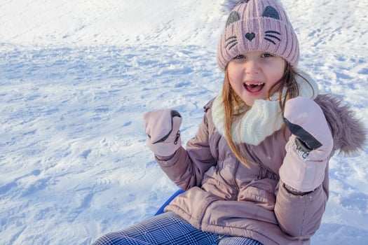 Young girl joyfully sledding down a snowy hill on a sunny winter day photo