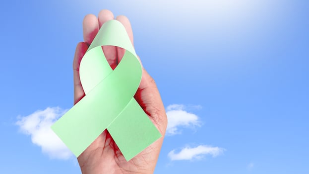 Hand holding green ribbon, symbolizing ovarain cancer awareness. Ribbon represents hope and unity, raising awareness and support for those affected by cancer, fostering understanding and prevention. photo
