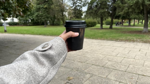 A hand holding a black coffee cup outdoors in Autumn season photo