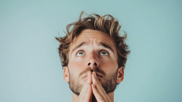 Young man with curly hair and a beard looking upward with a hopeful expression, reflecting deep thoughts against a light blue background photo