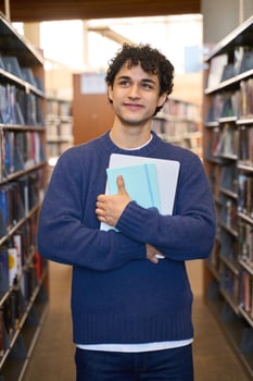 Thoughtful student holding books and laptop in library photo