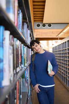 Young student leaning against bookshelf in library photo