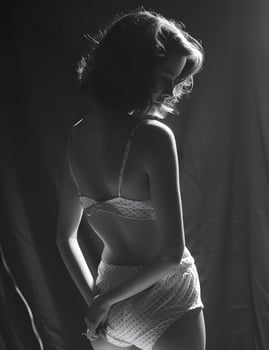 a black and white photo of a woman in lingerie standing in front of a curtain