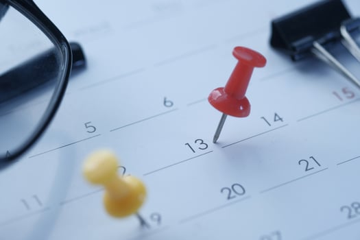 Brightly colored push pins affixed on a calendar, accompanied by a pair of reading glasses photo