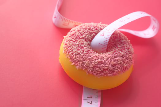 A colorful donut with a measuring tape placed over it on a delightful pink background photo