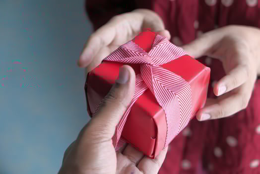 A Heartwarming Gift Exchange Moment Hands Gently Passing a Beautifully Wrapped Red Present photo