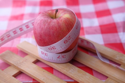 A Juicy Apple Carefully Wrapped in Bright Measuring Tape on a Colorful Checkered Background photo
