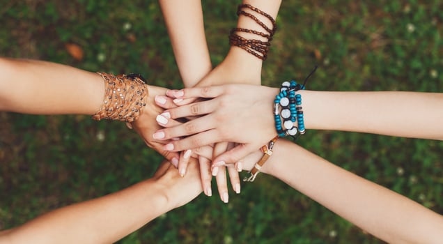United hands of young females, top view. Stylish hands of girlfriends in boho hippie bracelets at green grass background. Togetherness and support, youth fashion and active lesiure. Women friendship photo