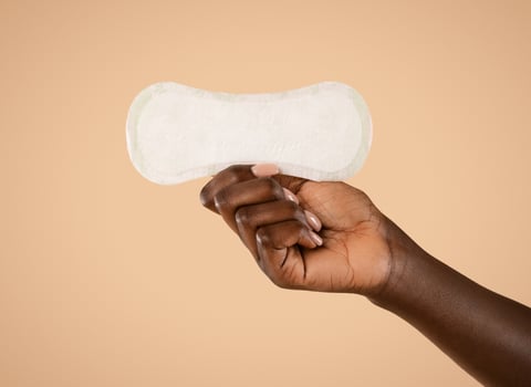 Unrecognizable african american woman hand holding daily pad, posing over beige studio background, isolated, cropped, copy space. Female period and intimate hygiene, menstrual products concept photo