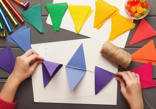 Birthday handmade background. Female hands making party paper decorations and colorful flags garland. DIY accessories on gray wooden planks, top view. Holiday organization, hobb, handicraft concept photo