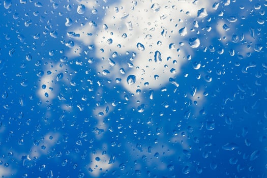 Rain drops on a window with blue sky background photo